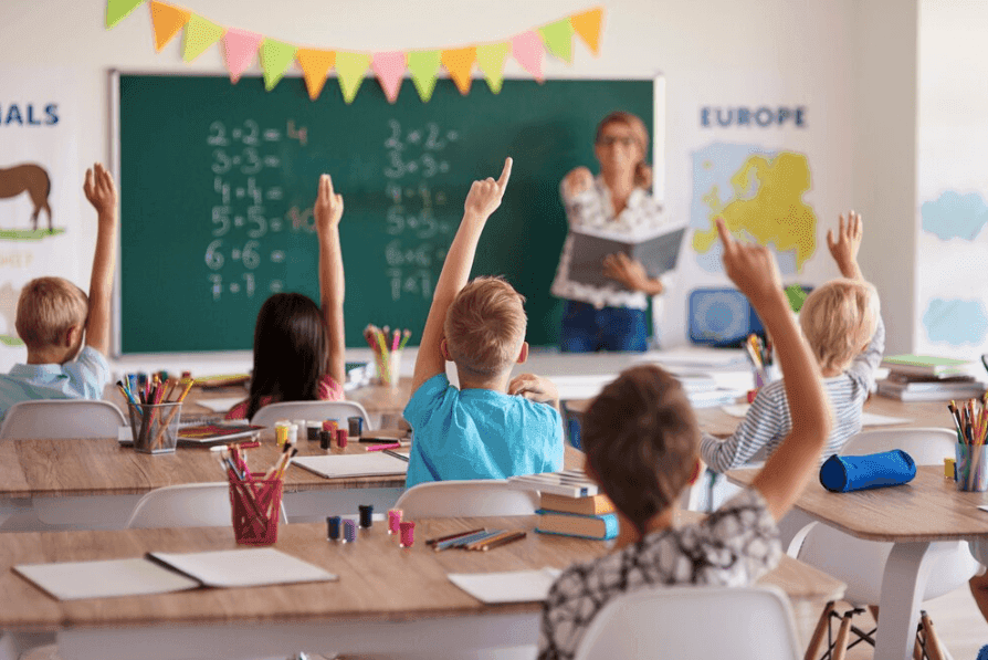 élèves d'élémentaire assis en classe et levant le bras face à la maîtresse